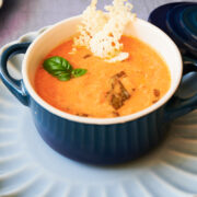 navy blue ramekin of creamy tomato soup with cheese crisp on top.