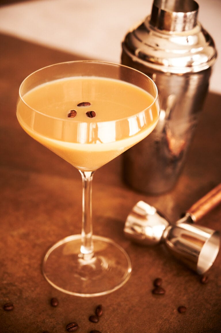 cocktail shaker and jigger with a coffee bean topped espresso martini.