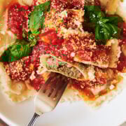 a fork with a bite of meat ravioli with red sauce and fresh basil