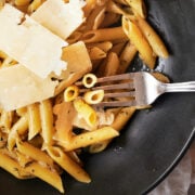 black bowl of penne pasta with parmesan shards and fork with a bite