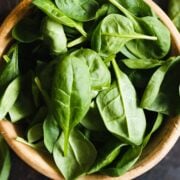 wooden bowl filled with fresh basil leaves on dark background