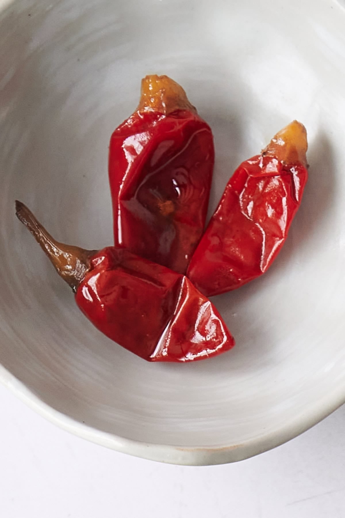 Three dried Calabrian chile peppers on a white ceramic plate, perfect for arrabbiata pasta sauce.