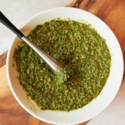 pesto in a white bowl with a muddler on a wooden board