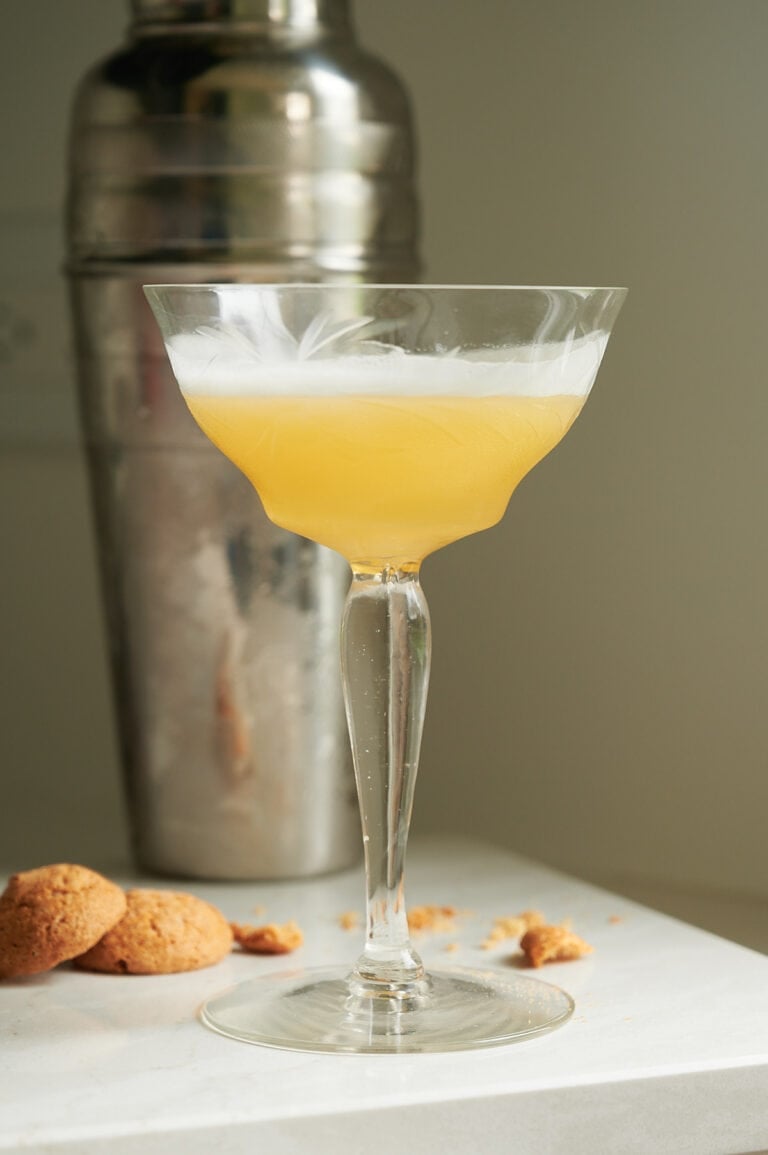 amaretto sour in a etched coupe glass with amaretti cookies and shaker.