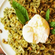 white platter of pesto pistachio bow tie pasta with burrata and fresh basil leaves.