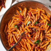 large skillet of sun-dried tomato pasta with a serving fork sprinkled with fresh basil and parmesan cheese.