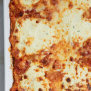 a corner of a white baking pan cheese topped baked ziti