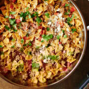 large skillet of Italian sausage and peppers pasta and a cheese grater and cheese