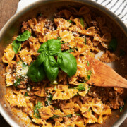 skillet of sausage pasta with creamy spinach sauce and basil leaves and wooden paddle