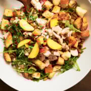 overhead view of a white bowl of peaches and chicken panzanella with bread cubes and arugula.