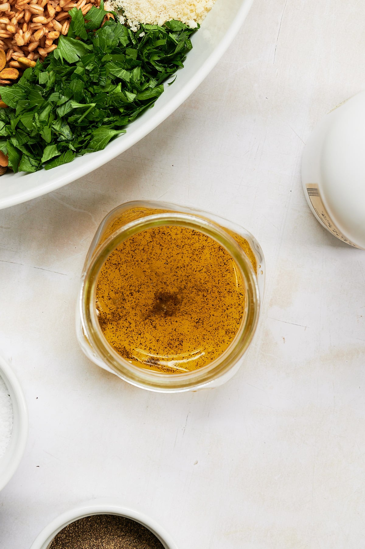 jam jar with lemon vinaigrette and white bowl of farro pilaf