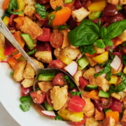 closeup of panzanella salad being scooped by an antique silver spoon in white bowl.