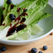 close up of white bowl with salad and blueberry balsamic dressing and blueberries sprinkled on wooden board