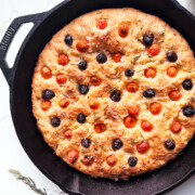 black skillet of baked focaccia barese topped with tomatoes, black olives and rosemary