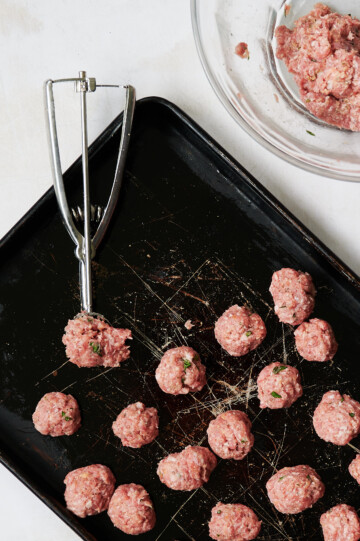 meatballs being scooped by cookie scoop on baking sheet
