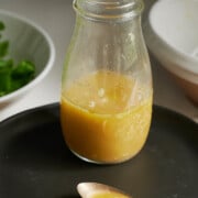 clear bottle of white balsamic vinaigrette sitting on a black plate with a spoon of dressing on it