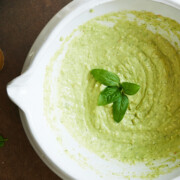 white bowl of creamy pesto dressing with fresh basil leaves on top