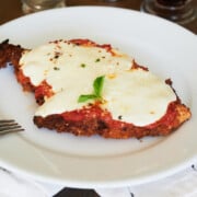 tablescape of white plate and fork with large piece of crispy chicken parmesan garnished with basil