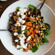 large white serving bowl of salad greens topped with roasted eggplant, butternut squash, feta and pistachios