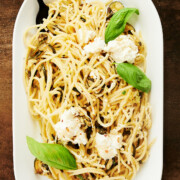 Long white platter with black spoon serving caramelized zucchini with ricotta and basil.