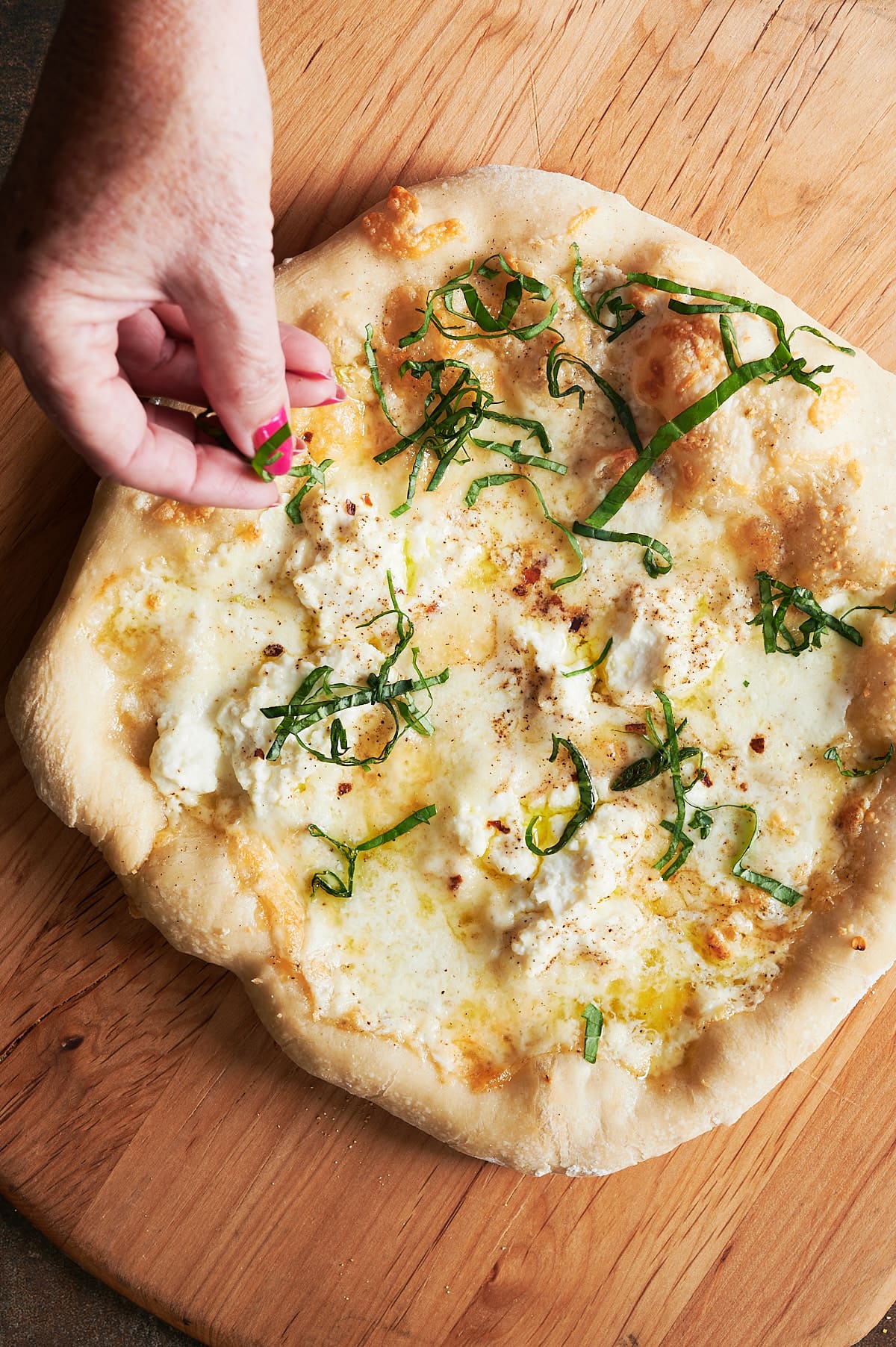 A hand sprinkled finely sliced fresh basil on a baked white pizza sitting on a pizza peel.
