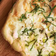 Baked finished white pizza topped with fresh julienned basil on a wooden pizza peel.