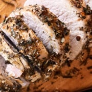 sliced boneless pork roast fanned on a wooden cutting board with a knife.