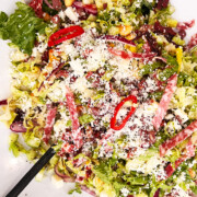 tossed antipasto salad in a white bowl with rings of peppers, salami and lots of parmesan