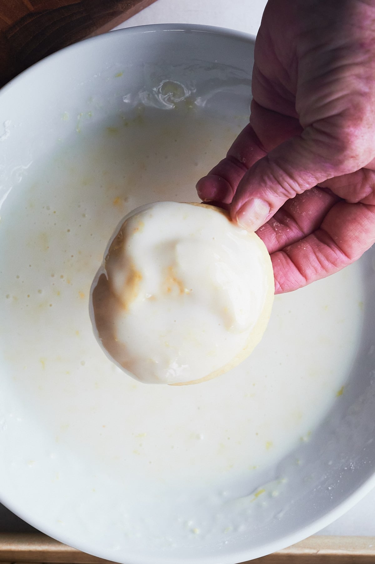 hand dipping lemon knot cookie into glaze.