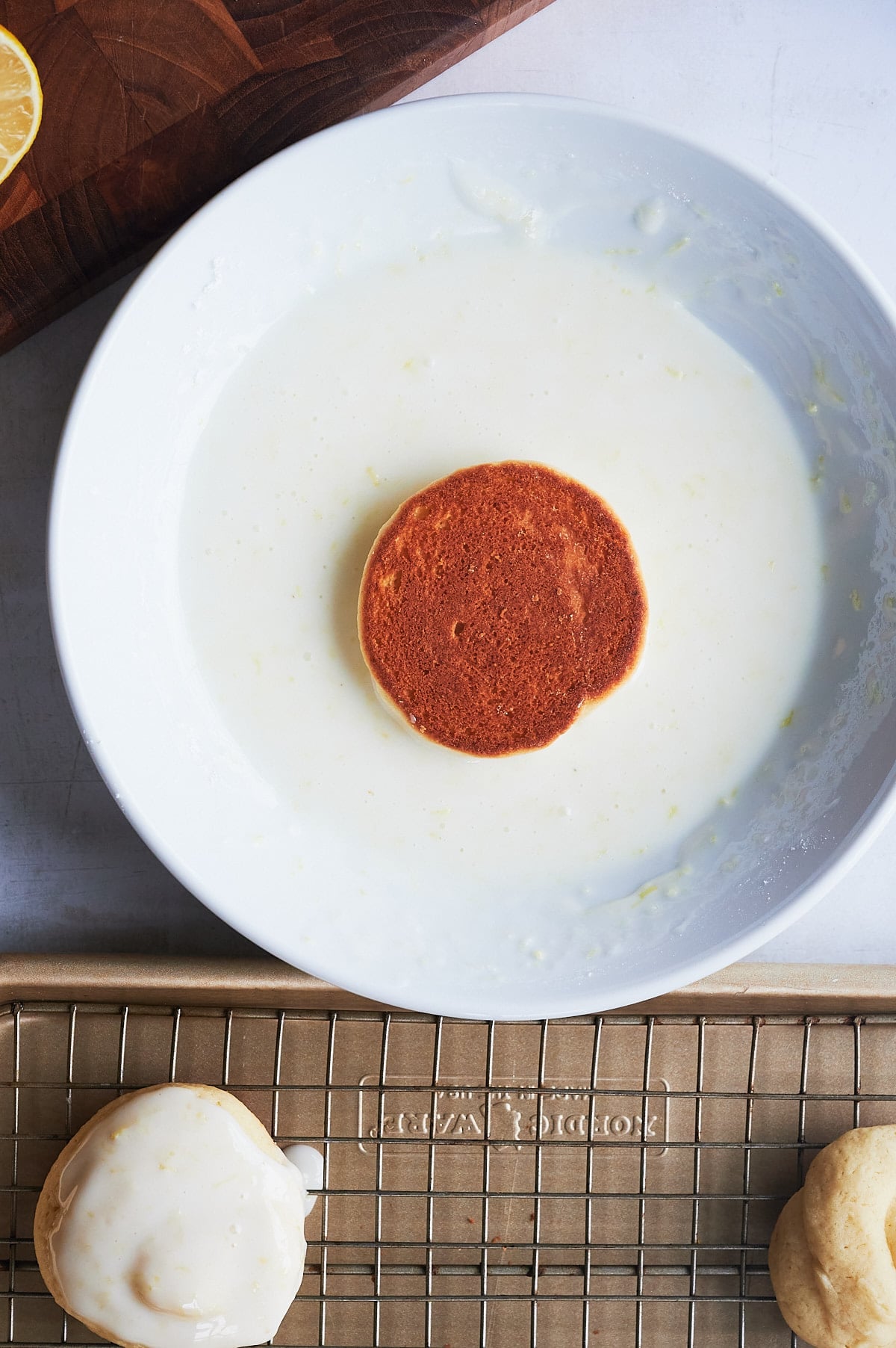 white plate of lemon glaze with lemon knot being dipped in glaze.