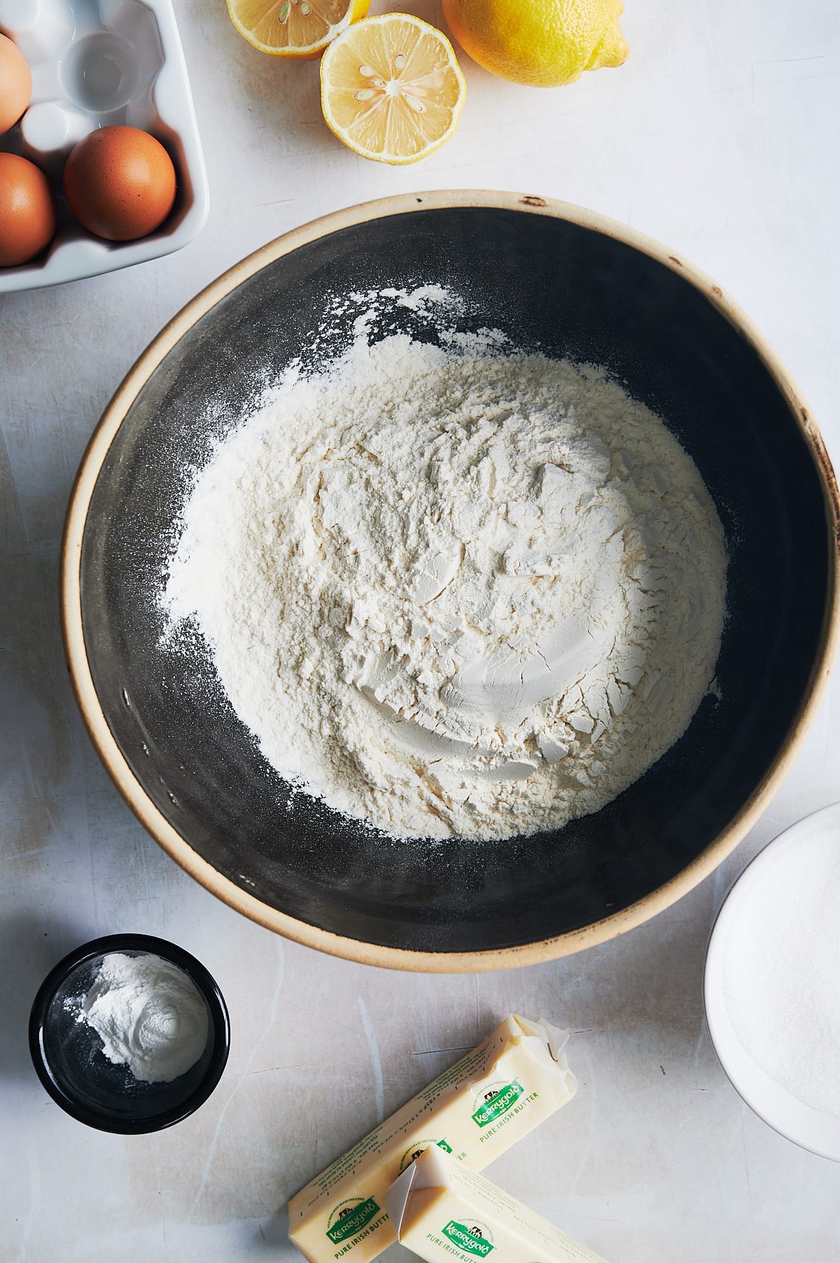 black bowl of dry ingredients, lemons, eggs, butter for lemon knots