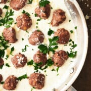 close up of skillet of meatballs Alfredo topped with parsley and parmesan.