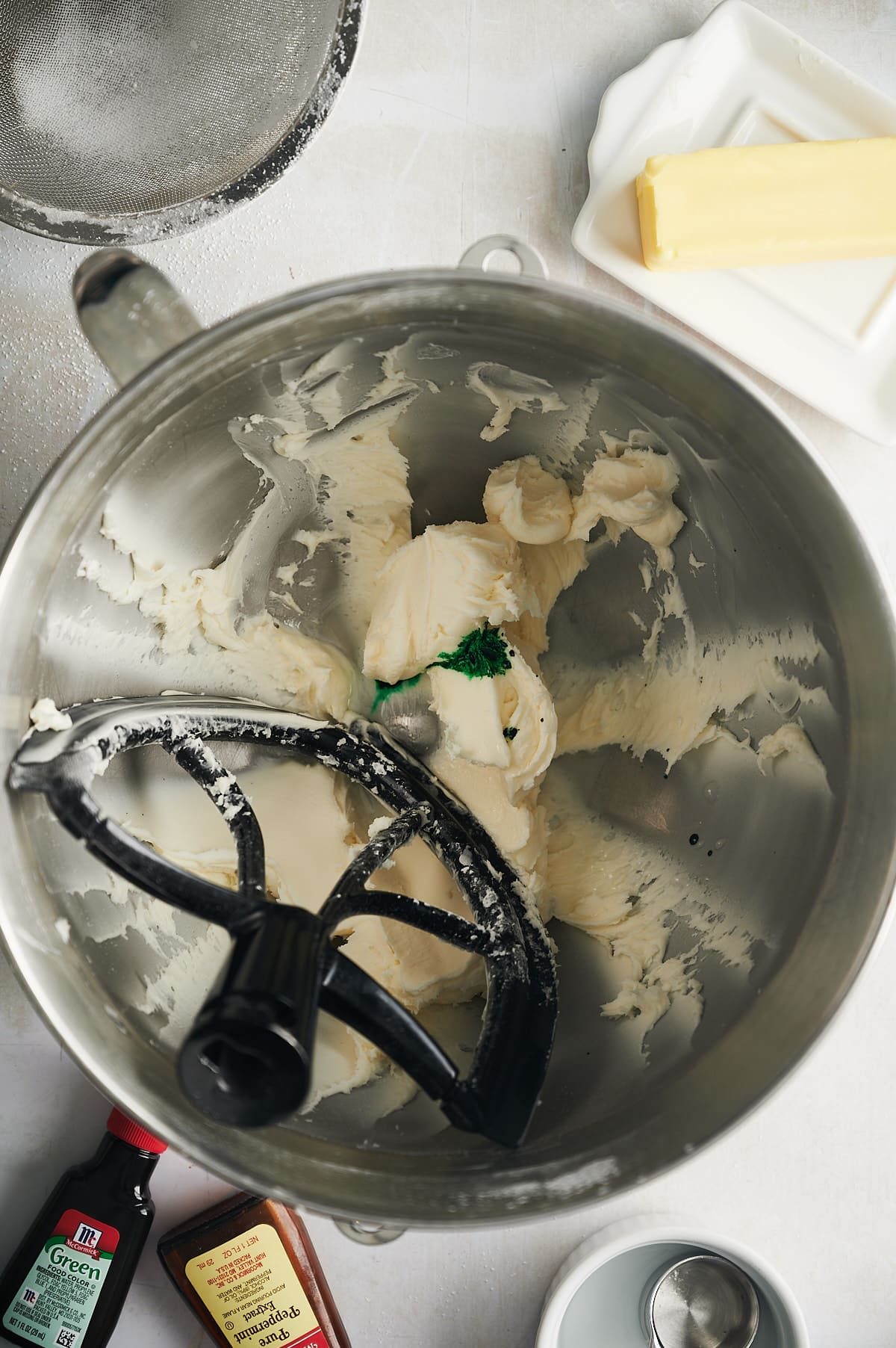 mixing bowl of confectioners sugar and butter with green food coloring.