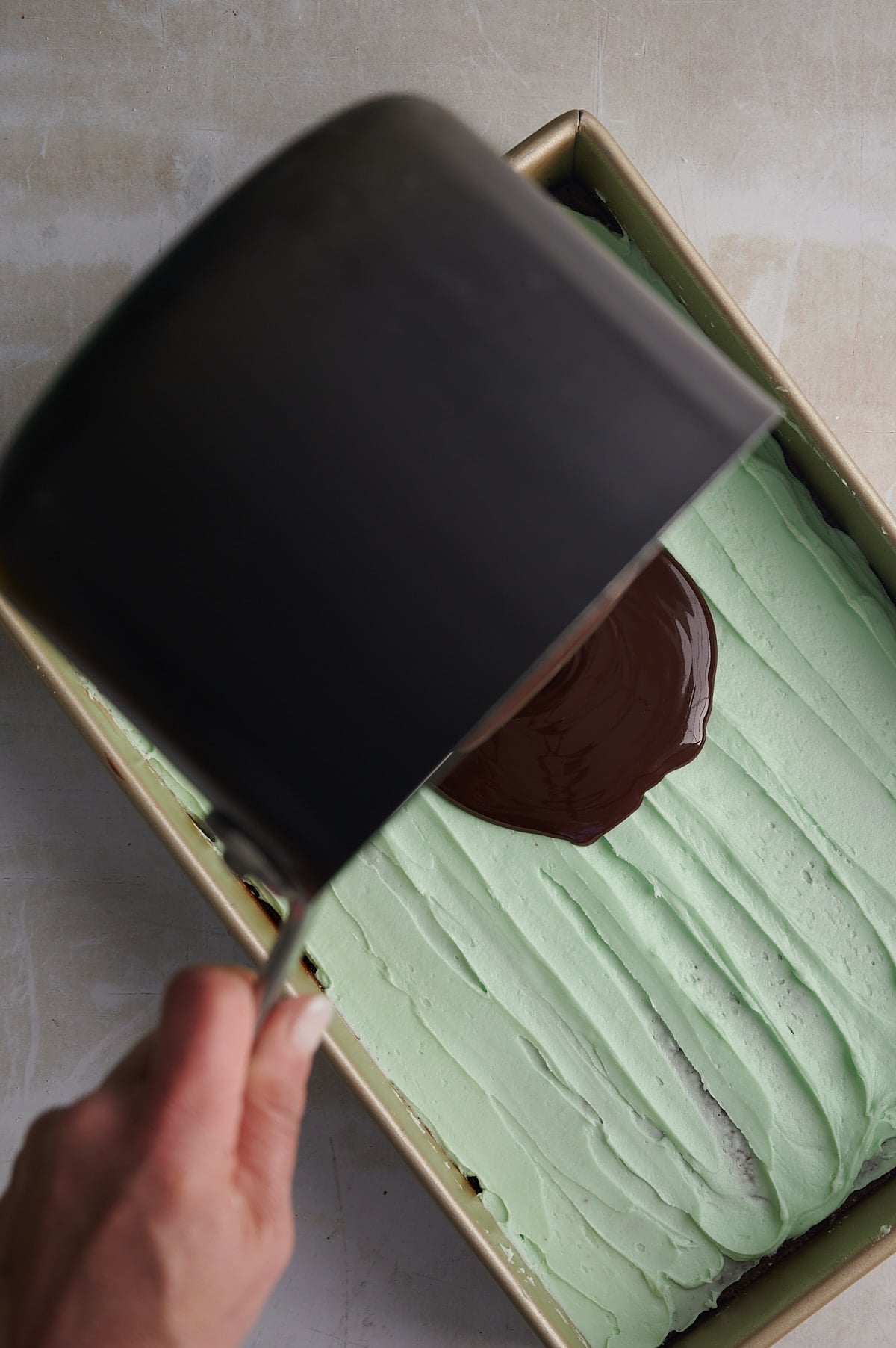 pouring chocolate ganache on mint layer of mint brownies.