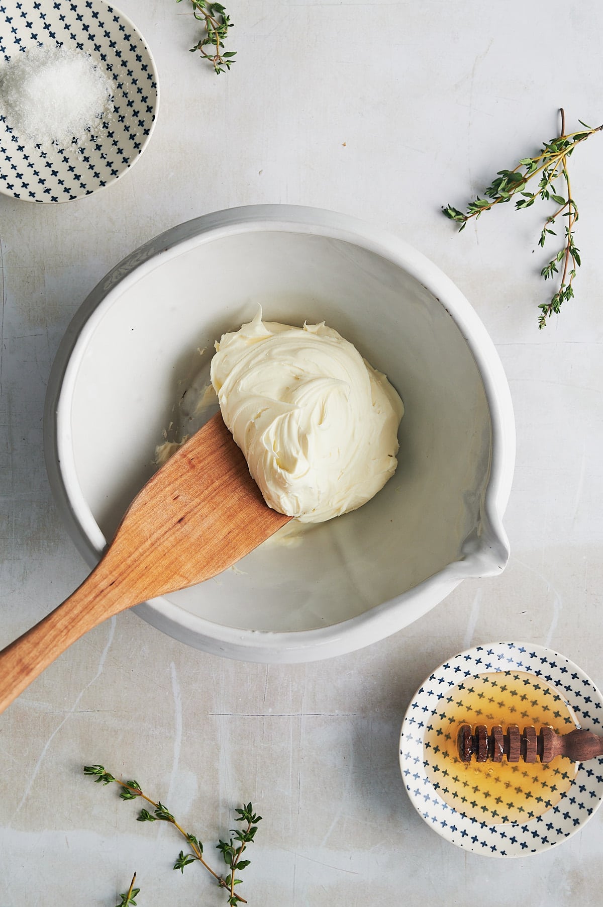 white bowl of mascarpone cheese with small bowls of honey and kosher salt and fresh thyme sprigs.
