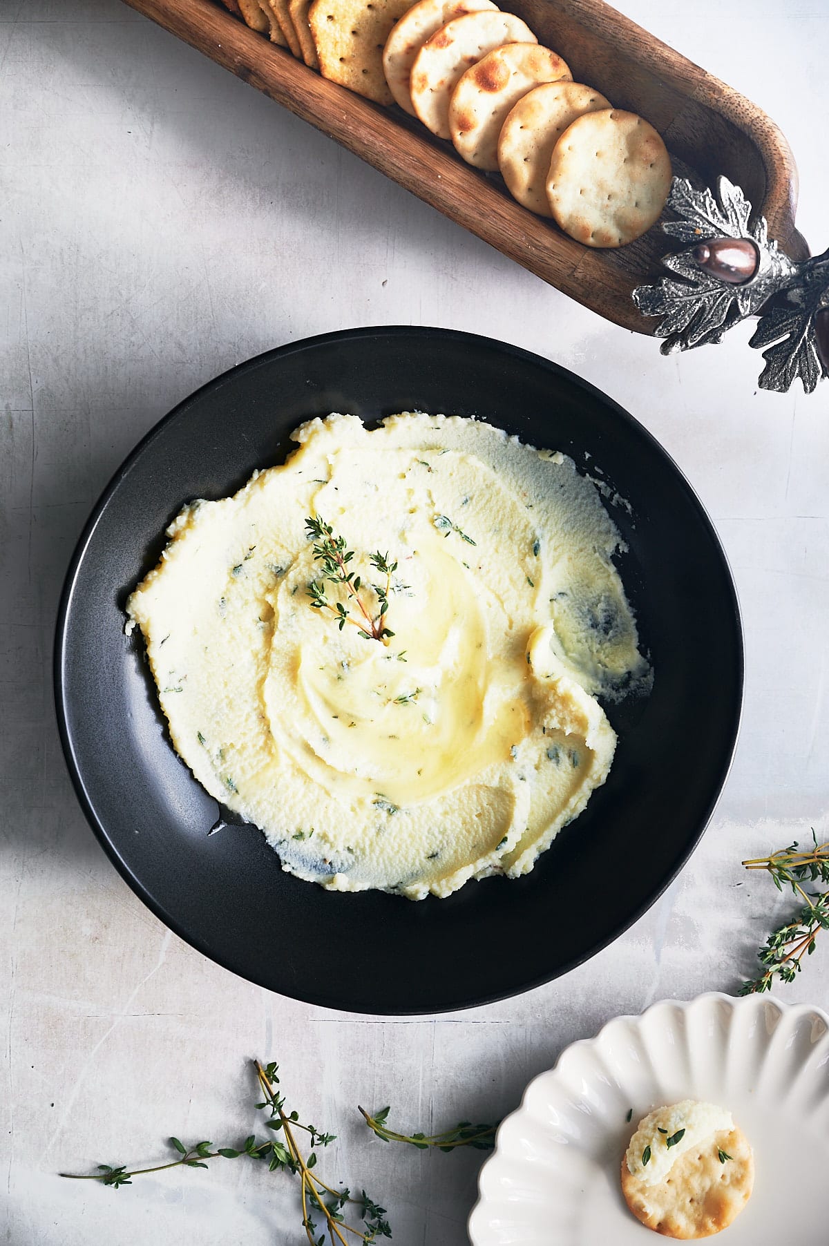 black bowl of honey mascarpone dip being served with crackers and fresh thyme sprigs.