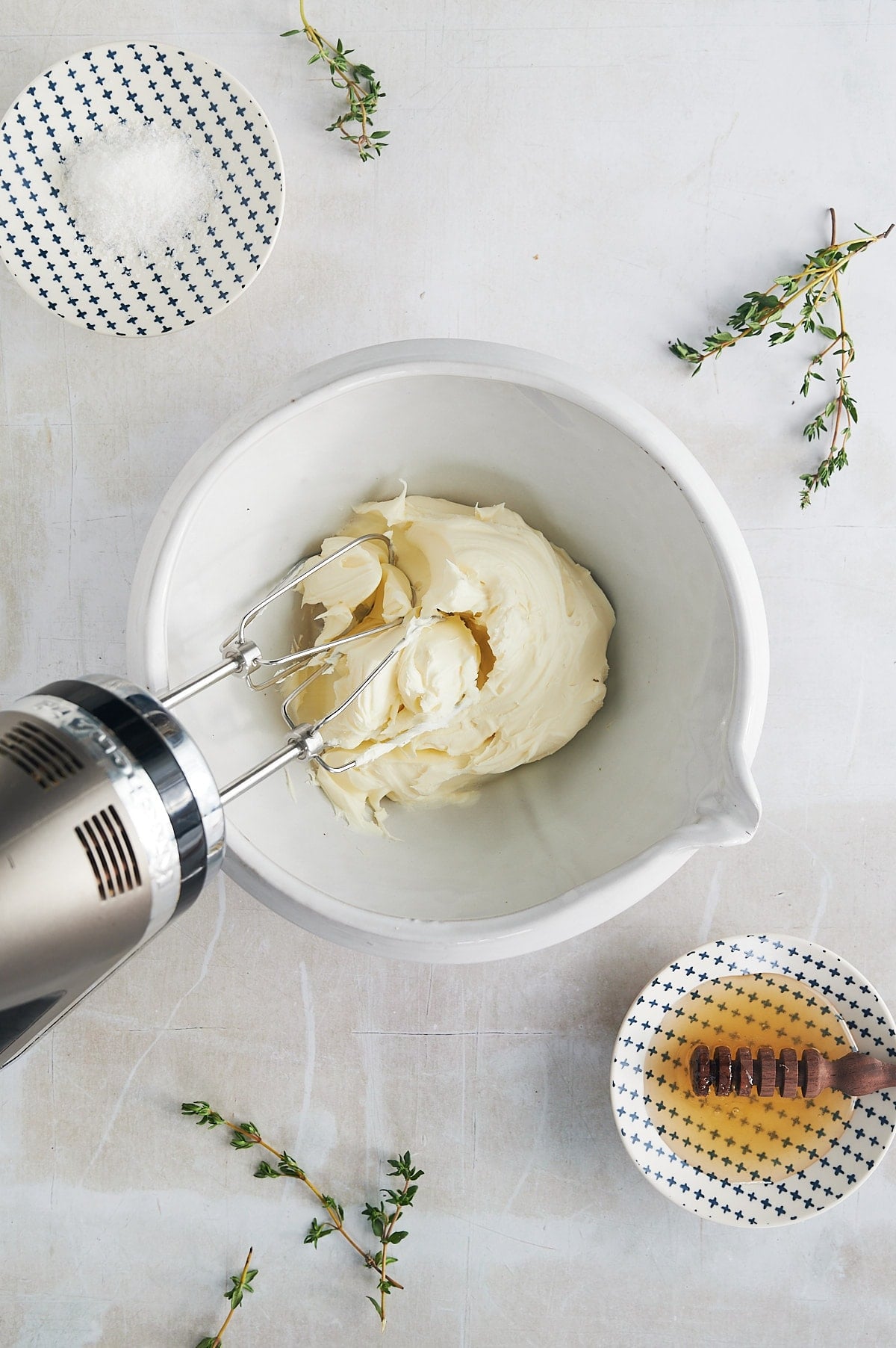 white bowl of mascarpone cheese being whipped with hand mixer.