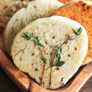 wooden bowl of lined up parmesan thyme crackers garnished with fresh thyme