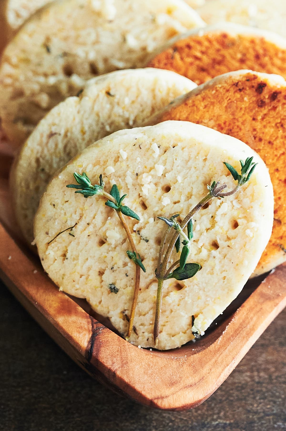 wooden bowl of lined up parmesan thyme crackers garnished with fresh thyme