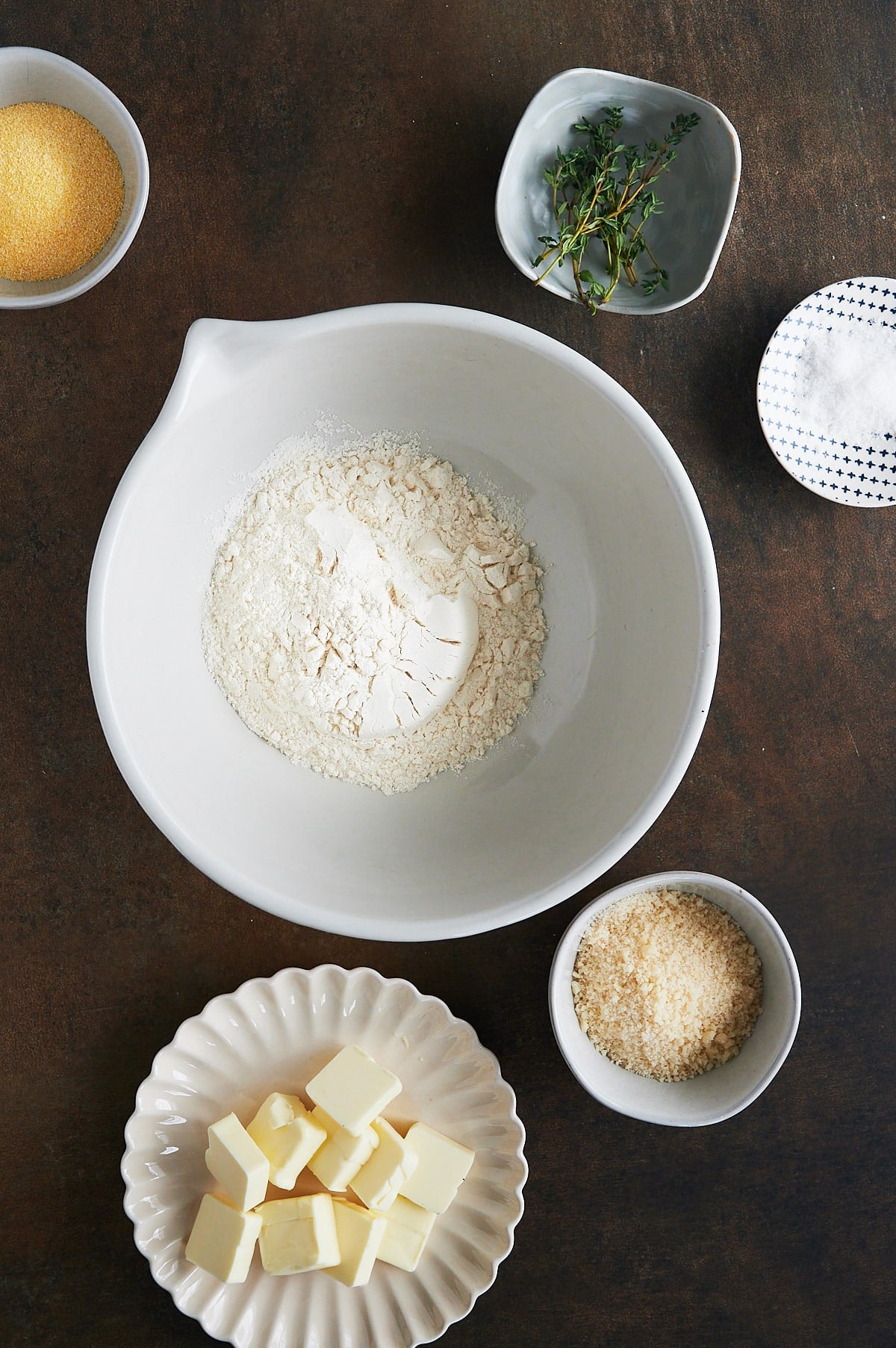 white bowl of flour and bowls of butter, parmesan, thyme and cornmeal.