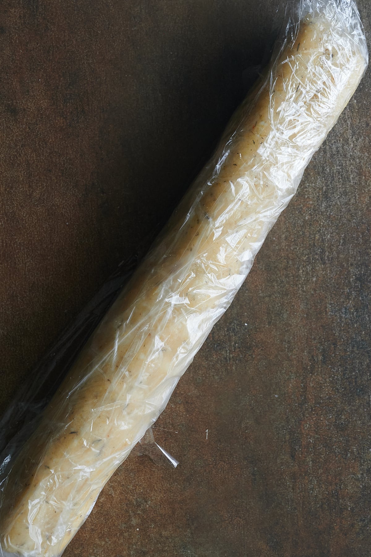 roll of parmesan thyme cracker dough wrapped in plastic wrap.