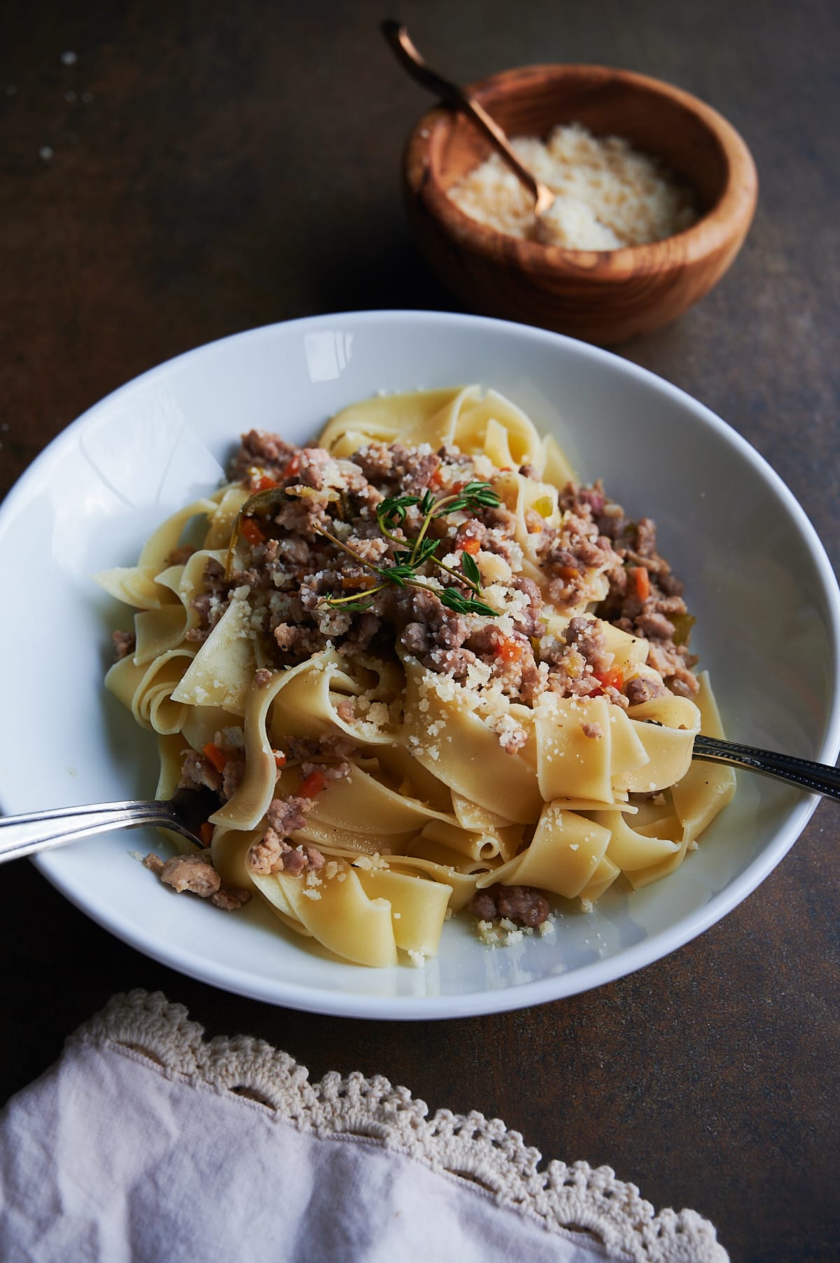 Lace napkin below a white bowl of chicken Bolognese sauce over pasta.
