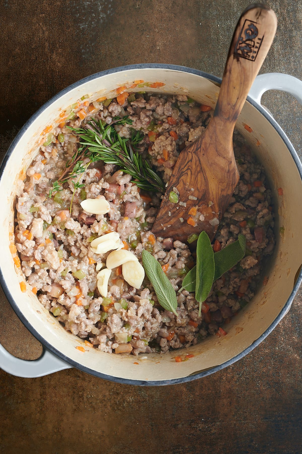 Adding fresh rosemary, garlic, sage and thyme to pan of white Bolognese.