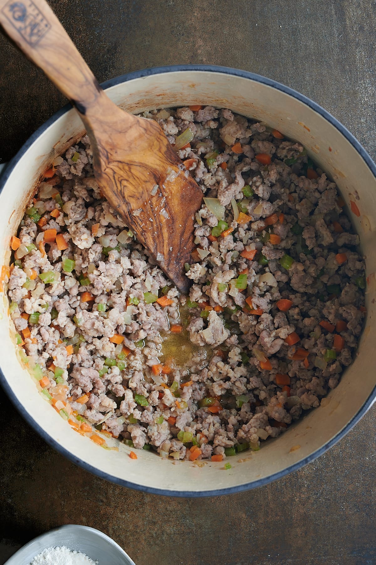 Cooked meats and vegetables in white Dutch oven on dark background