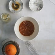 white bowl with salad dressing and shallots in it with bowls nearby on a white background