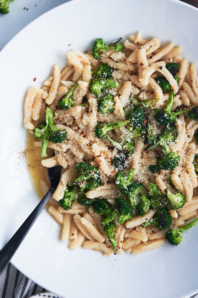 white bowl of cavatelli pasta and broccoli sprinkled with fresh parmesan and crushed red pepper.