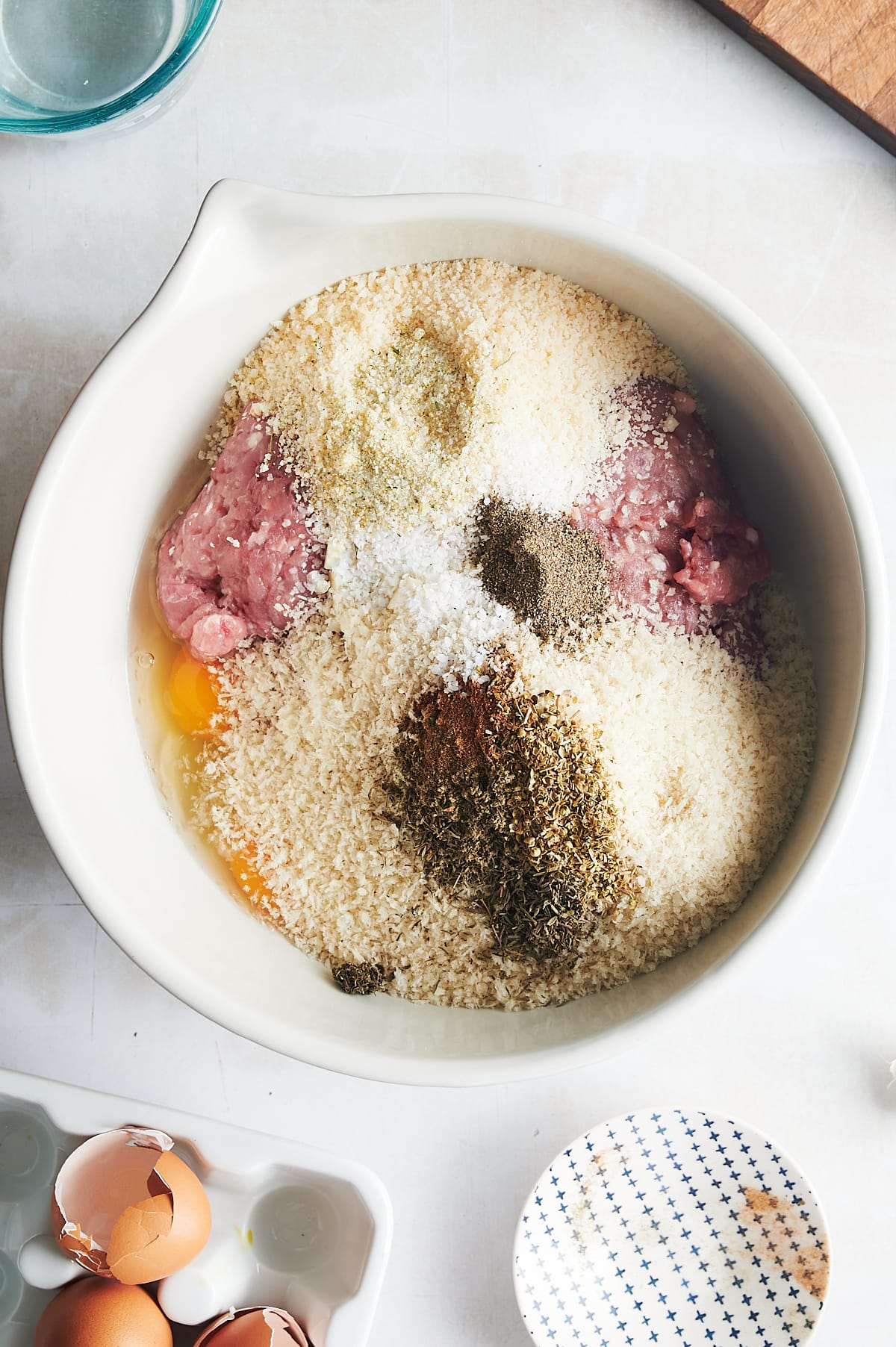 white bowl of panko and seasoning, herbs, eggs mixed in ground chicken.
