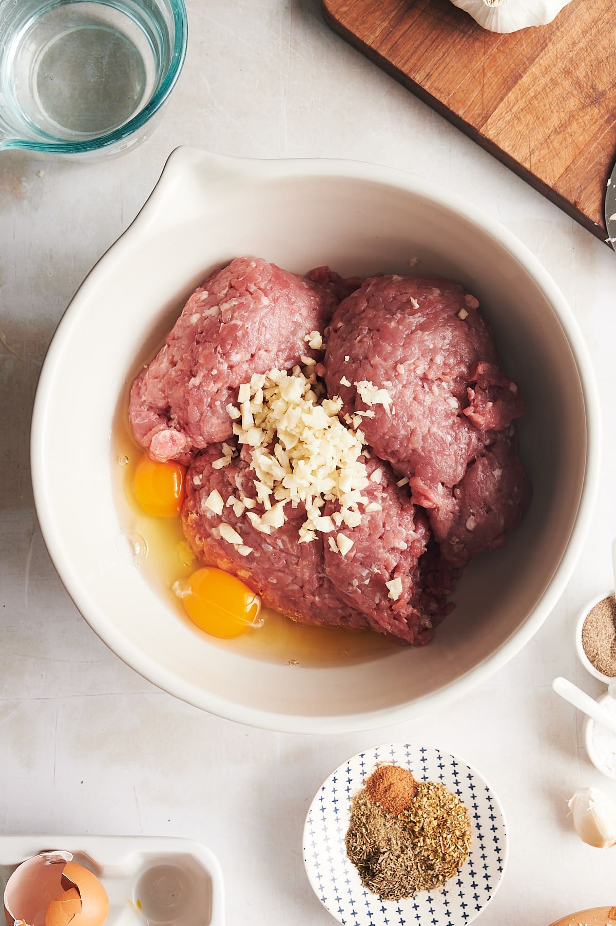 white bowl of ground chicken thighs and unbeaten eggs with minced garlic on top.