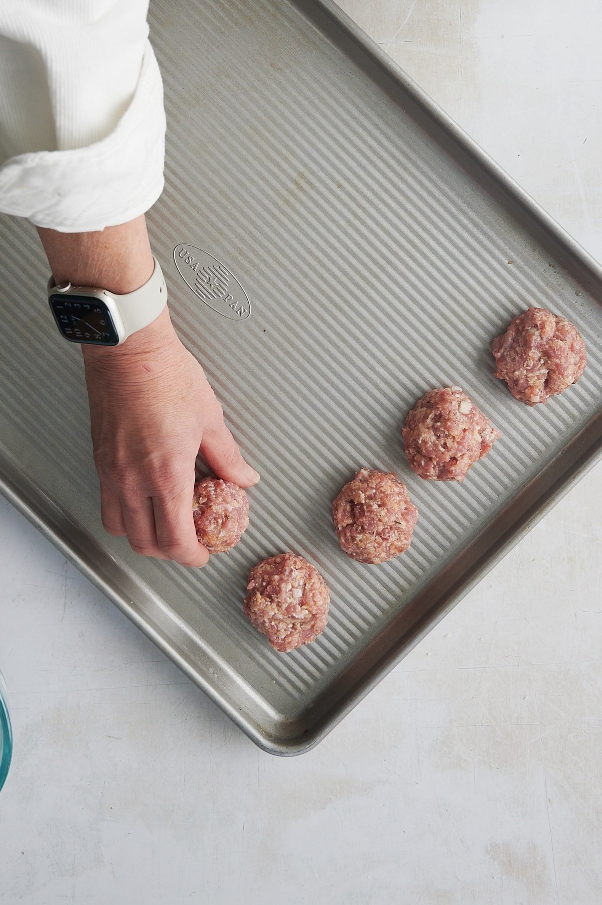 Sheet pan being filled with ground chicken thigh meatballs.
