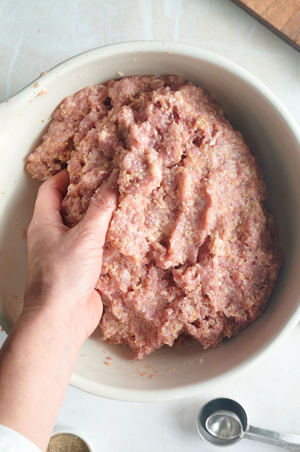 white bowl of chicken meatball mix being mixed with water by hand.